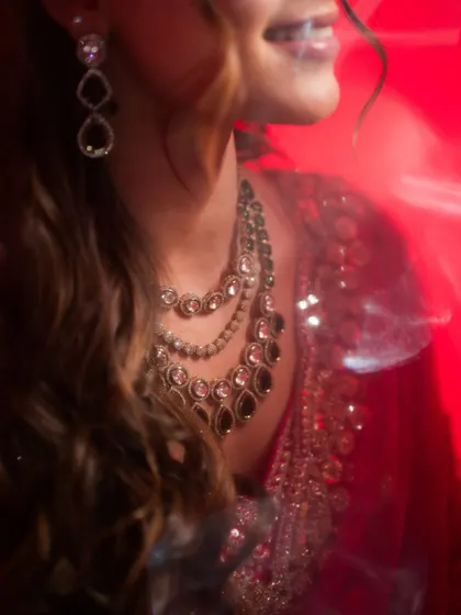 A close-up detail shot focusing on the bride's magnificent jewelry, with a creative red light flare adding a touch of glamour.