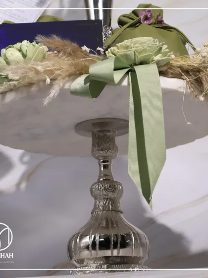 A close-up of the bespoke invitation for The Gourmet Fest, featuring a silver vase, pampas grass, and a custom-designed card, all set on a marble cake stand.