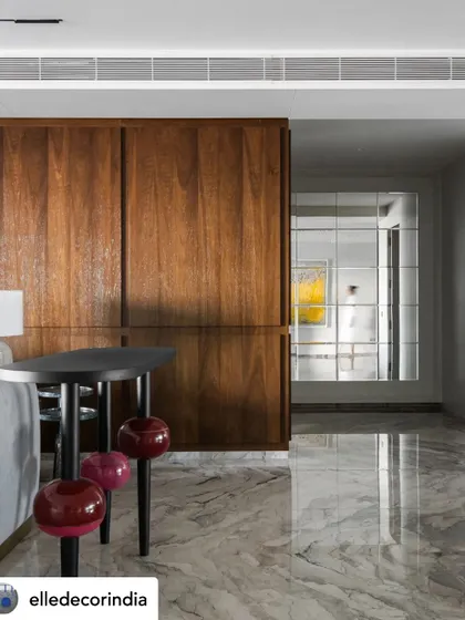 A detail of the living room, where the rich wood paneling meets the sleek marble floor. The reflection shows a glimpse of a yellow art piece, highlighting the home's layered and colorful personality.