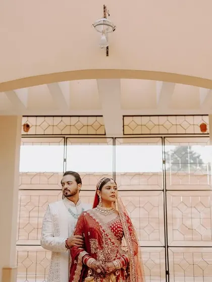 A regal portrait of the bride and groom, standing under an archway in a palace-like venue, looking like royalty.