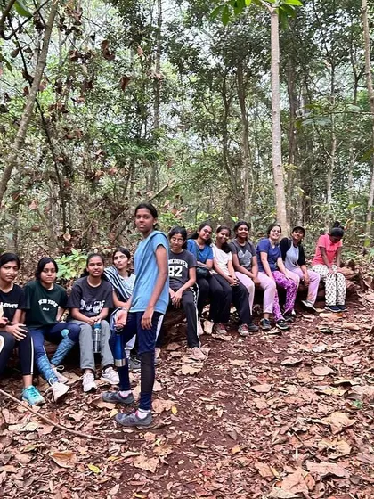 A group of girls takes a break on a fallen log during a nature walk, enjoying the serene forest environment.