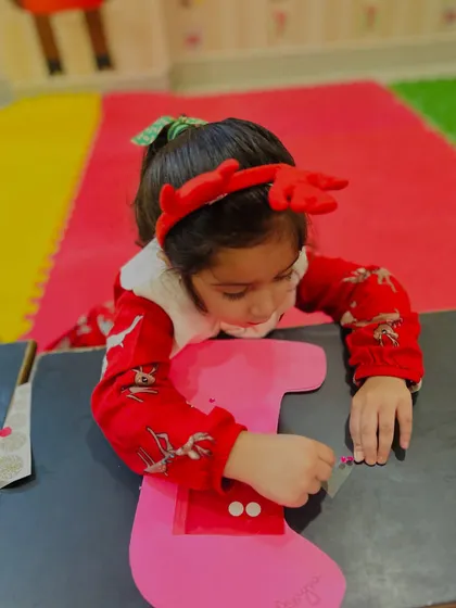 A girl concentrates on decorating a large pink Christmas stocking craft.