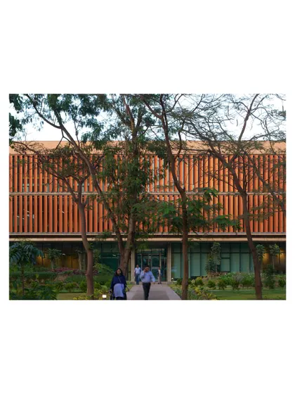 Pedestrians walk through the landscaped grounds of the JSW Vijayanagar campus, with the modern administrative building in the background. The design prioritizes people, with pathways weaving through mature trees and lush greenery.