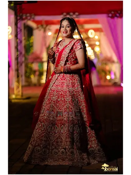 A beautiful full-length portrait of the bride, capturing her smile and the elegance of her red lehenga.