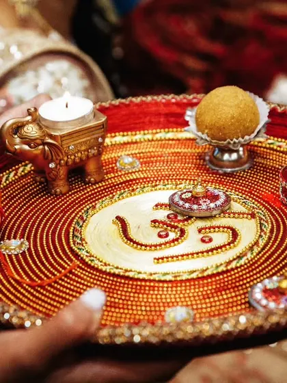 A close-up of a beautifully decorated puja thali, featuring the 'Om' symbol, a diya, and other ritual items.