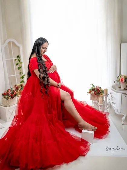 A full-length view of this magnificent red tulle gown. This pose is designed to showcase the dress and create a sense of graceful power for the mother-to-be.