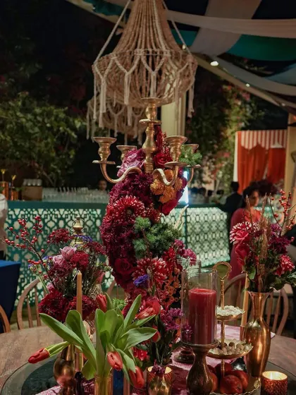 A tablescape from the event, featuring a grand floral centerpiece in a brass candelabra, set under a macrame chandelier. The design blends rustic, bohemian, and Moroccan elements for a unique look.