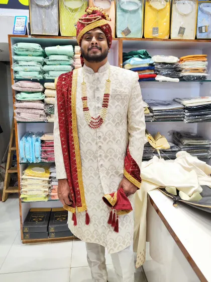 A full view of our ivory sherwani, showcasing its intricate embroidery and how it pairs beautifully with a red pagdi and a matching embroidered stole for a complete groom's look.