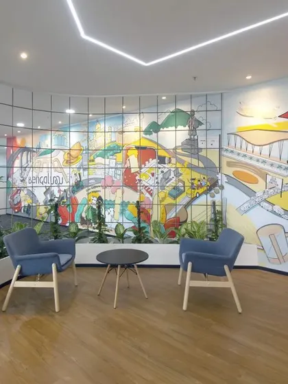 A waiting area at Scientific Games featuring a large, colorful mural that captures the spirit of Bengaluru. The comfortable seating and biophilic elements create a pleasant and engaging space for visitors.