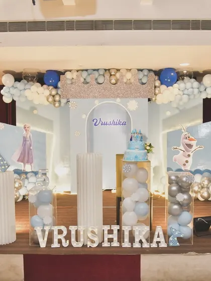 A grand Frozen-themed stage with transparent balloon-filled pillars and a glittering crown centerpiece.