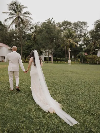 The couple walks away hand-in-hand, the bride's long veil trailing behind her, creating a romantic and cinematic image.