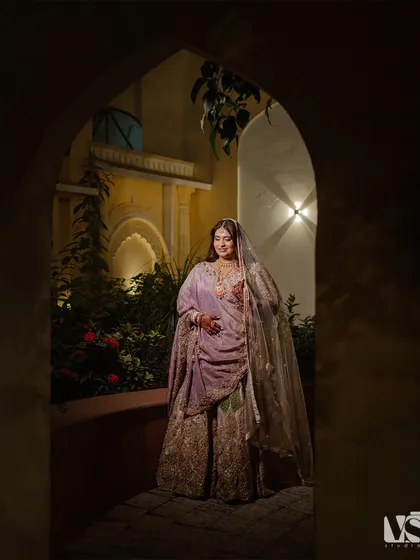 Sonal framed within a traditional Rajasthani archway. The play of light and shadow creates a dramatic and regal portrait, highlighting her lavender lehenga and the beautiful architecture.