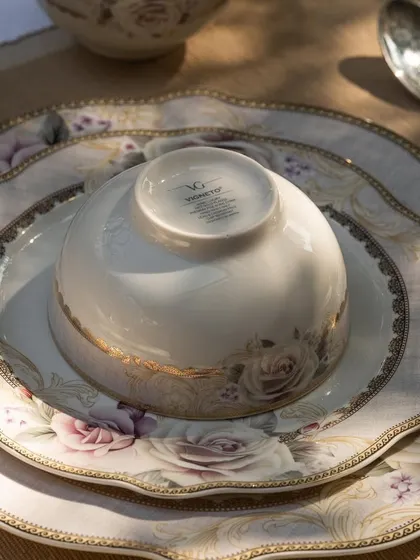 A beautifully lit shot of Vigneto's rose-patterned dinnerware. The sunlight catching the gold rim of the plates highlights the luxurious quality and fine details of the collection.