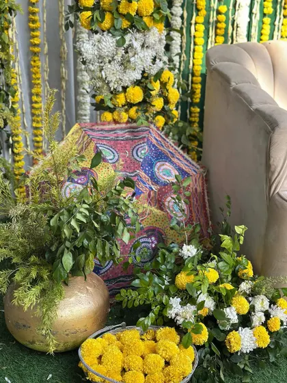 A close-up of the decor elements for the outdoor Haldi. This shot highlights the use of fresh marigolds in baskets and brass pots, alongside a decorative umbrella.
