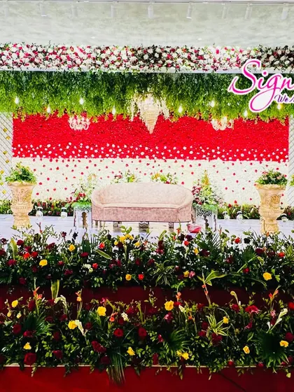 For this reception, I created a backdrop with a wall of red and white flowers arranged in a dotted pattern. The stage is framed with a lush green floral border and small chandeliers.