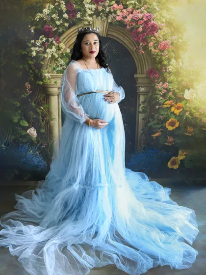 A full-length portrait of a mom-to-be in a flowing light blue gown and tiara, looking like a queen in our studio.