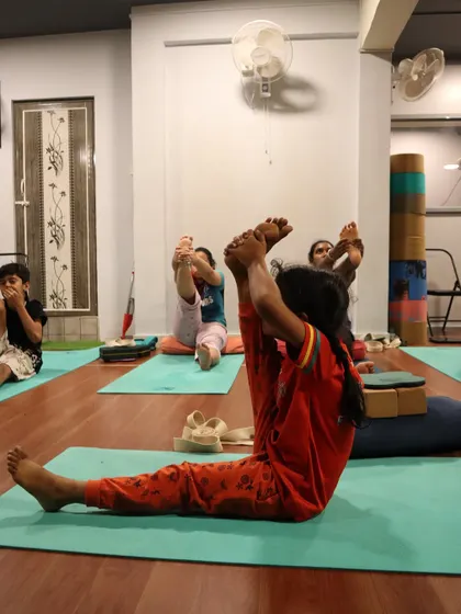 Students practice a seated forward bend variation, working on hamstring flexibility and focus.