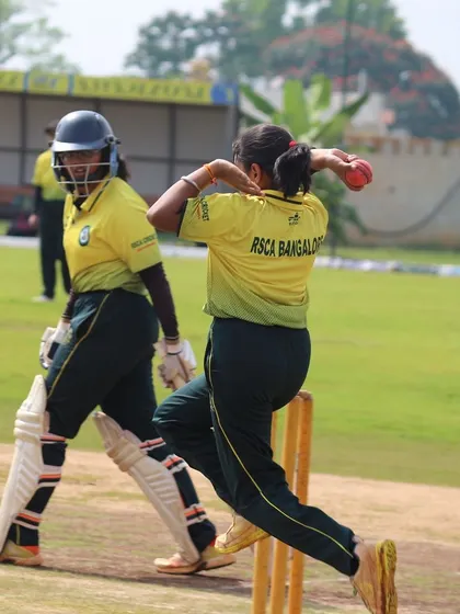 A bowler completes her follow-through as the non-striker looks on.