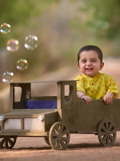 A happy passenger in a rustic toy truck. The addition of bubbles adds a touch of whimsy and fun to this sunny outdoor baby photoshoot.