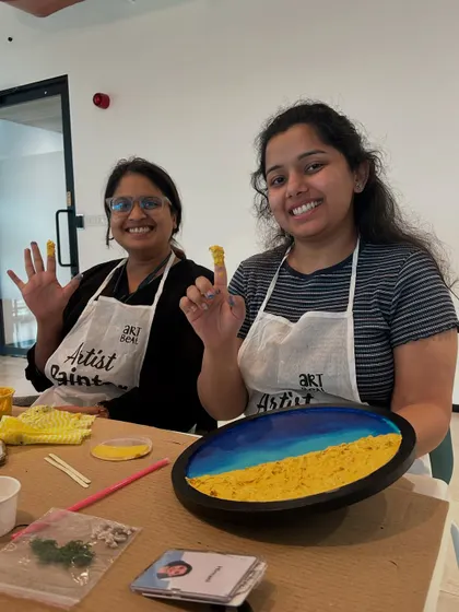Two participants from the Samsara tech workshop showing off their messy, paint-covered hands and their finished art. It’s all part of the fun.