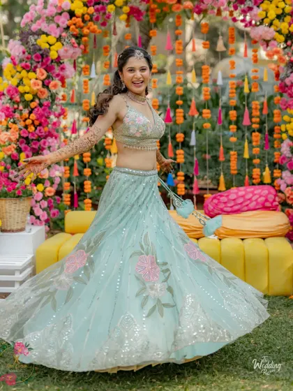 A joyful twirl from the bride at her Mehendi, showcasing her beautiful lehenga against the vibrant floral decor.
