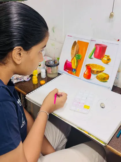 A student carefully studies a reference image to understand the composition and color scheme for her still life painting. We teach students how to deconstruct and replicate complex arrangements.
