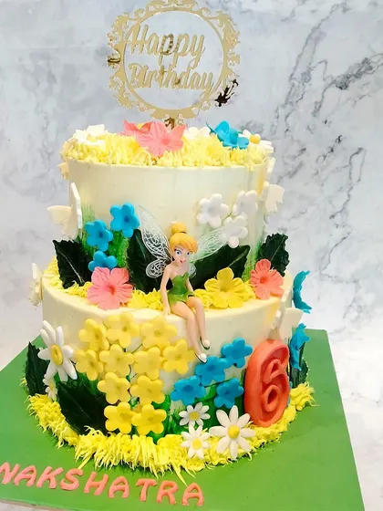 A beautiful two-tier Tinkerbell themed cake. The cake is set in a floral garden, with Tinkerbell sitting amongst the flowers.