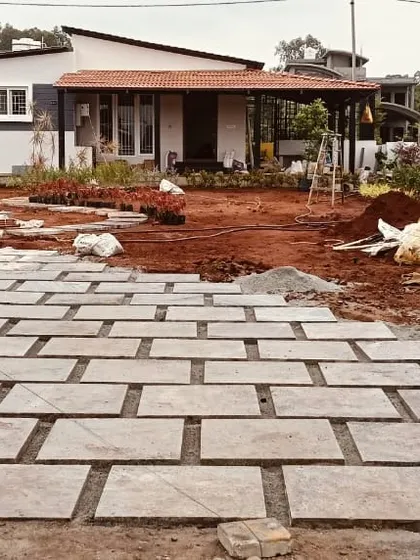 A view of a landscaping project from the main gate, showing the newly installed paver driveway and the surrounding area being prepared for planting.