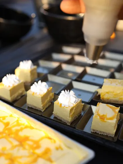 Our pastry chefs carefully prepare bite-sized portions of mango cheesecake. Each piece is meticulously crafted and garnished, perfect for pass-around service at any event.