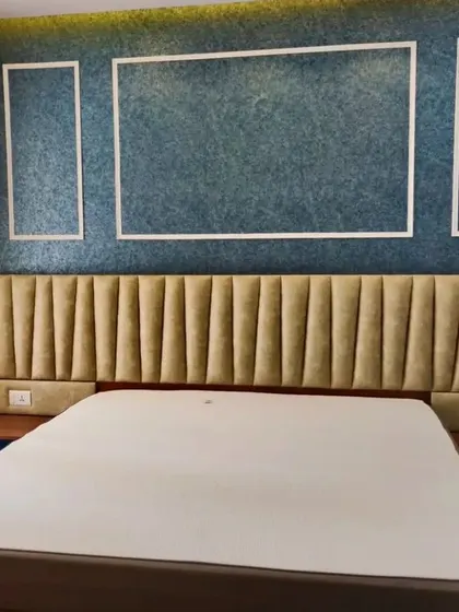A close-up of the bed and headboard, highlighting the contrast between the textured blue wall and the soft, channel-tufted headboard.