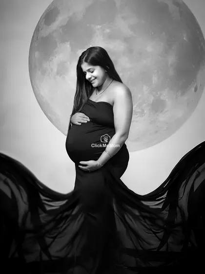 A serene and beautiful black and white portrait with the moon backdrop. The flowing black gown creates a stunning contrast, emphasizing the beauty and power of the mother's form.