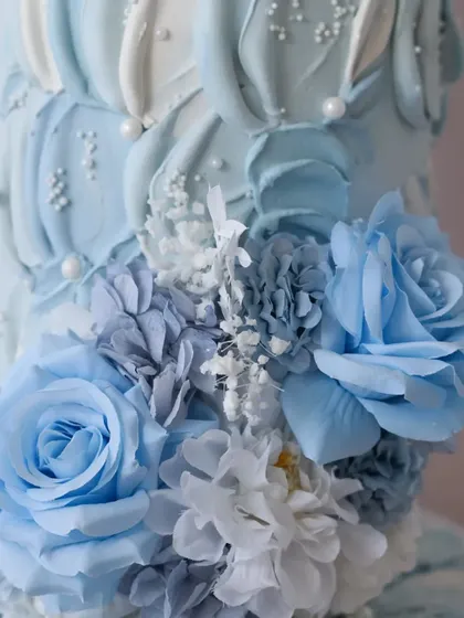 A close-up of the sugar flower arrangement, showing the mix of blue roses and white hydrangeas.
