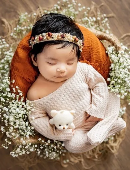 A peaceful newborn nestled in a rustic basket, surrounded by baby's breath and holding a tiny teddy. These posed shots are perfect for capturing their angelic features.