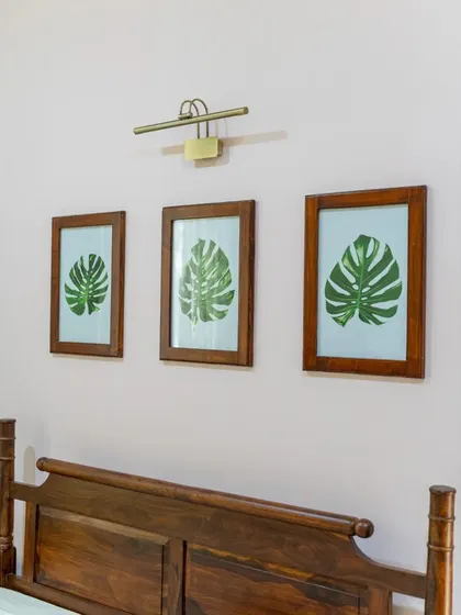 A close-up of the framed monstera leaf prints above the bed, which serve as the focal point and reinforce the room's sylvan theme.