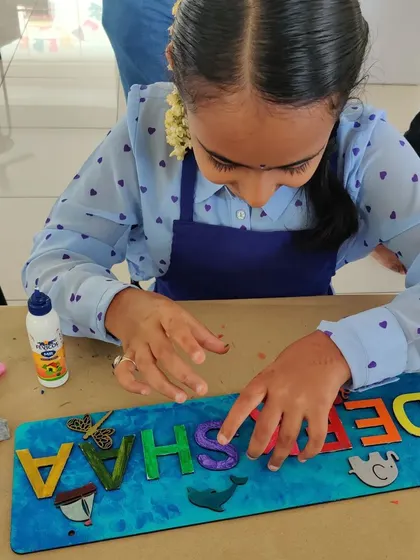 A young girl concentrates on gluing colorful letters and shapes onto her wooden nameplate, a popular activity at our birthday parties.