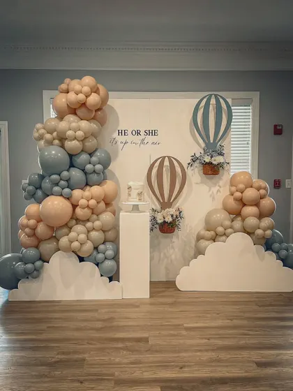 The full "Up in the Air" gender reveal setup. The pastel blue and pink balloons and hot air balloon props create a sense of anticipation and fun.