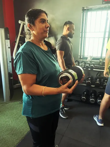 A client holds a dumbbell, focused and ready for her next set, while others train in the background.