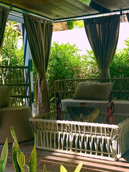 A close-up view of the pergola's interior, showing the comfortable daybed and unique woven chairs. The design details create a feeling of being in a high-end resort.