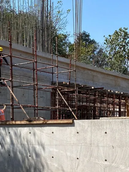 Workers on scaffolding alongside a long concrete retaining wall at the farmhouse site. This wall helps to shape the landscape and create different levels in the garden.