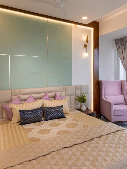 This luxurious bedroom features a pastel green accent wall with metallic inlay, paired with a comfortable pink wingback chair. The combination of soft colors and rich textures creates a chic and inviting retreat.