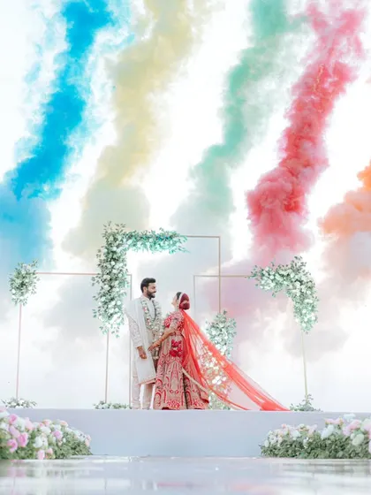 A spectacular shot of the couple on their wedding stage, framed by an explosion of rainbow-colored smoke bombs, creating a truly unforgettable moment.