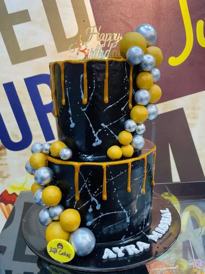 A striking 4kg two-tiered black cake with gold and silver drips and balloon decorations for a modern celebration.