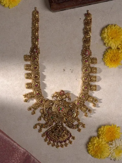 This magnificent bridal haram is a true showstopper. It features a large, ornate peacock pendant at its center, with layers of intricate gold-toned metalwork and colorful stone embellishments extending upwards.