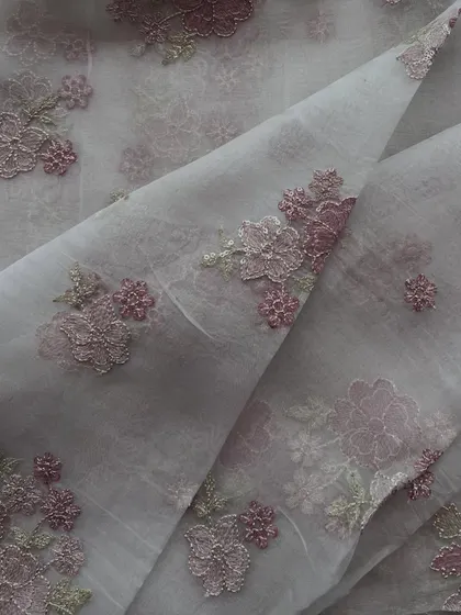 This embroidered organza features three-dimensional floral embroidery in shades of purple, adding a unique texture and depth to the sheer fabric.
