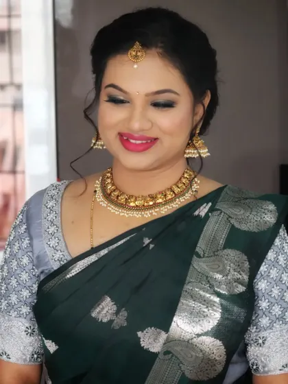 A sophisticated look for a housewarming party. The client is wearing a dark green saree with a modern silver blouse, and her makeup is kept elegant with a pop of pink on the lips.