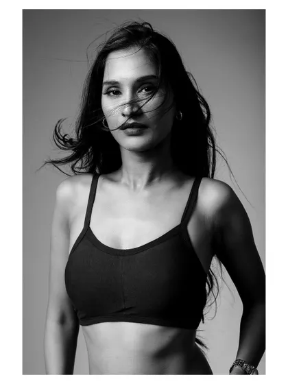 A black and white portrait of a model in activewear. The wind-blown hair and strong pose create a dynamic and powerful fitness shot.