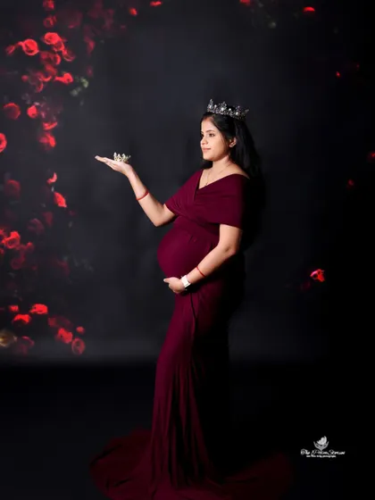A creative and regal portrait. The mom-to-be, wearing a crown, holds a smaller crown in her palm, symbolizing the little prince or princess on the way.