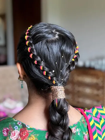 A unique and colorful braided ponytail. This style features a crown braid and a lower braid woven with bright pink and yellow threads, perfect for a vibrant Mehendi or Navratri look.