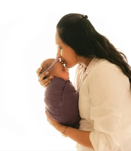 A mother gently kissing her sleeping, swaddled baby on the forehead.
