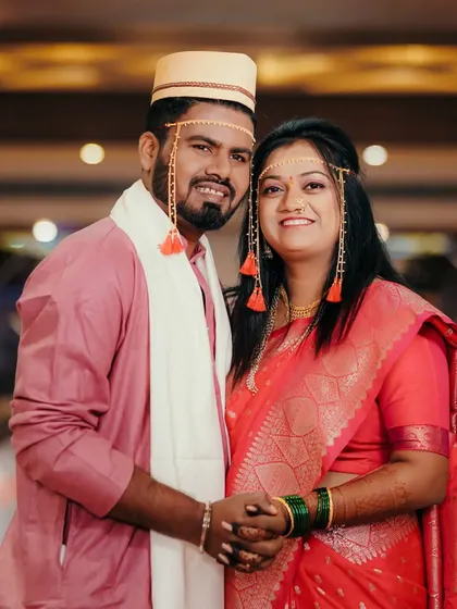 A classic portrait of the Maharashtrian couple, Sagar and Shraddha, holding hands and smiling for the camera. Their traditional attire, including the Mundavalya, is beautifully showcased.